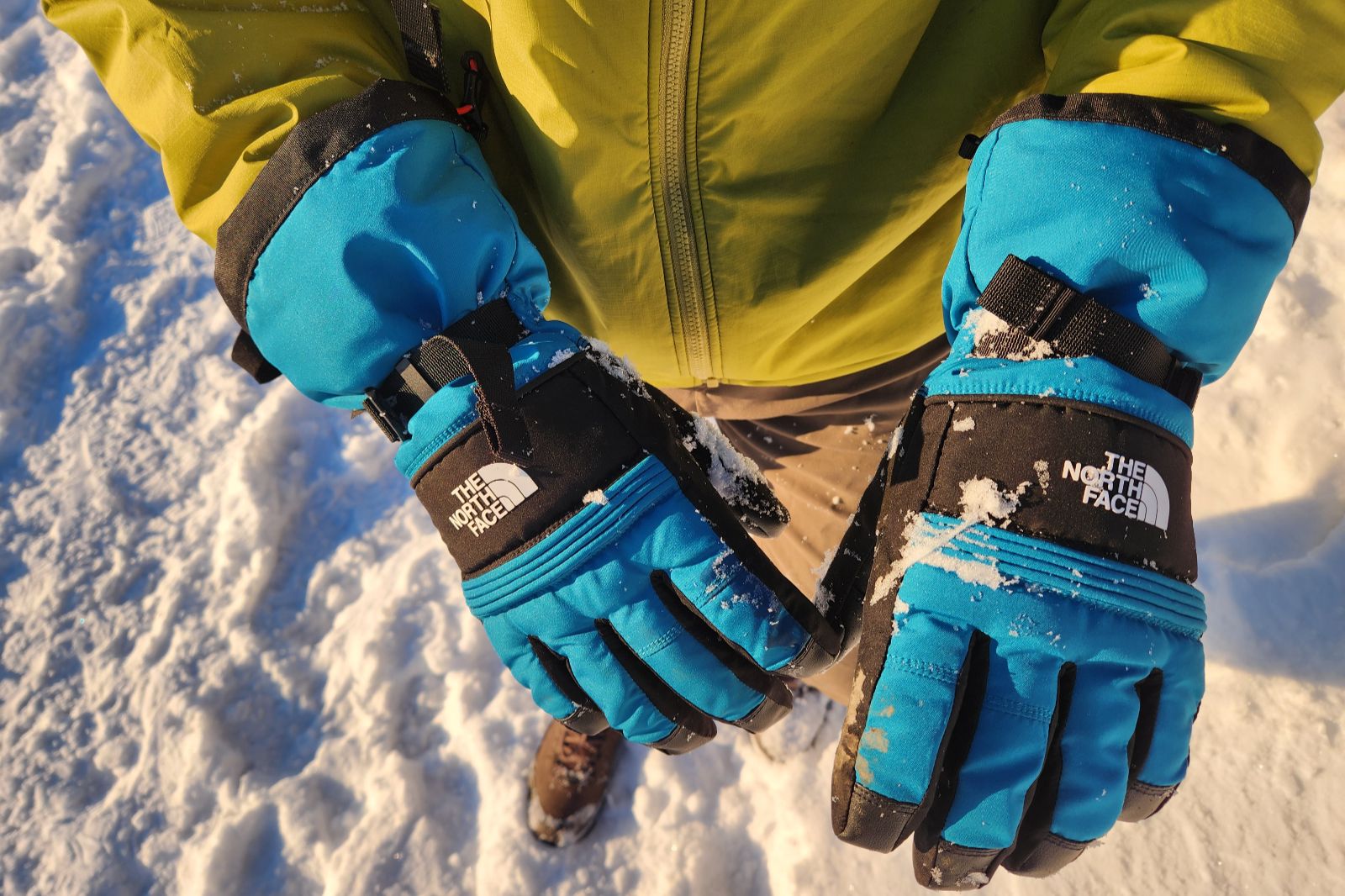 A pair of blue gloves with snow on them.