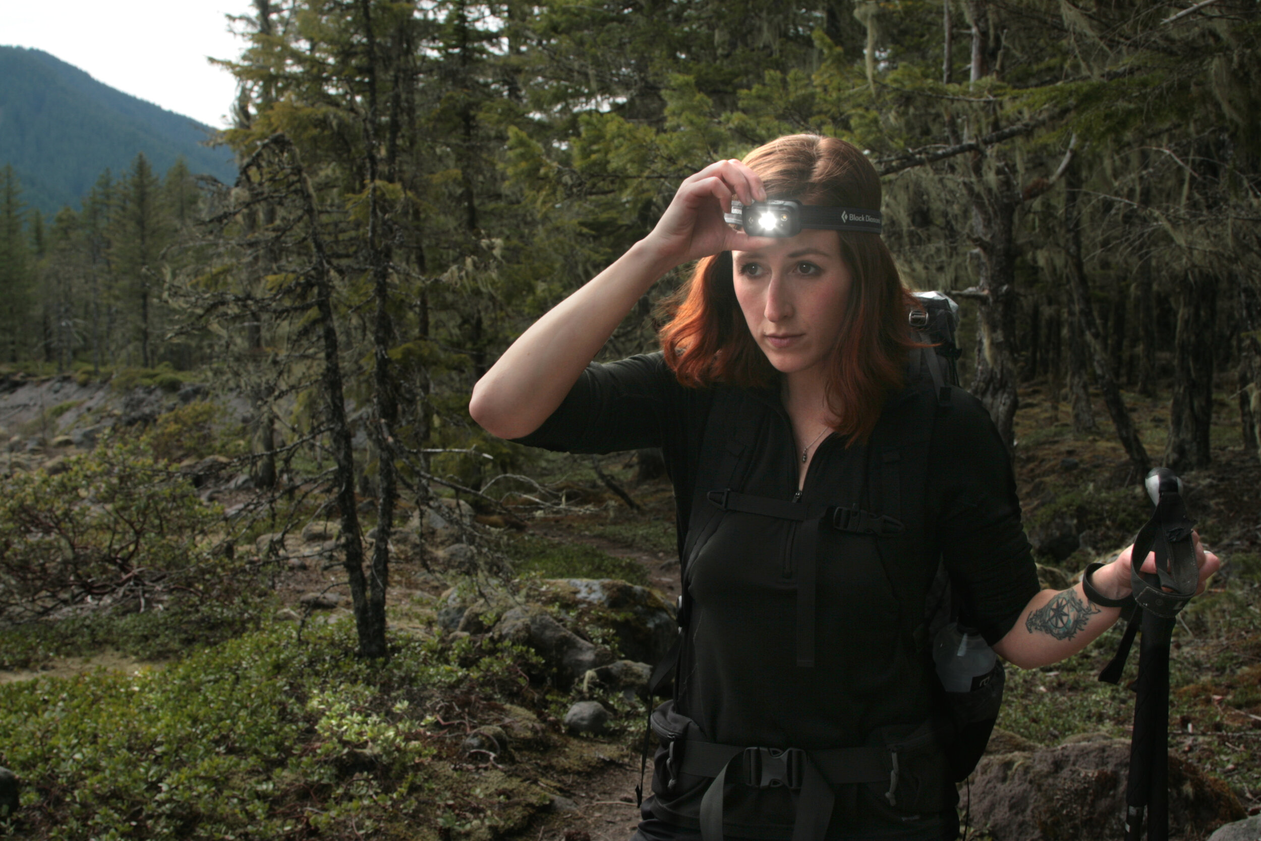 A hiker coming out of a forested section of trail with their headlamp on