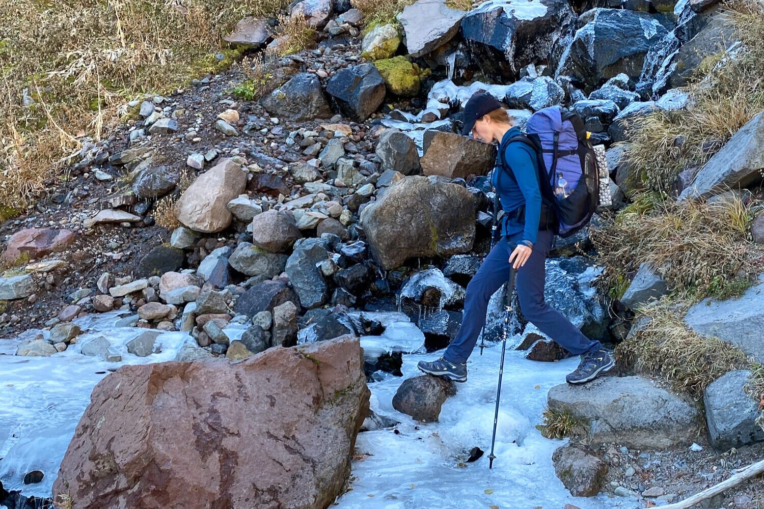 woman crossing a frozen creek using trekking poles to balance 