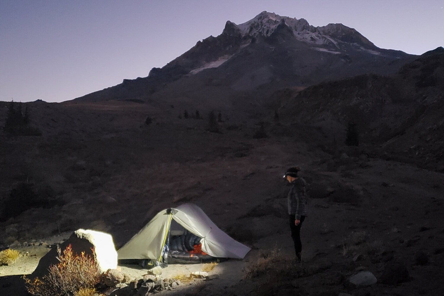 moonlit night at mt. hood wih a tent pitched with a headlamp casting its light