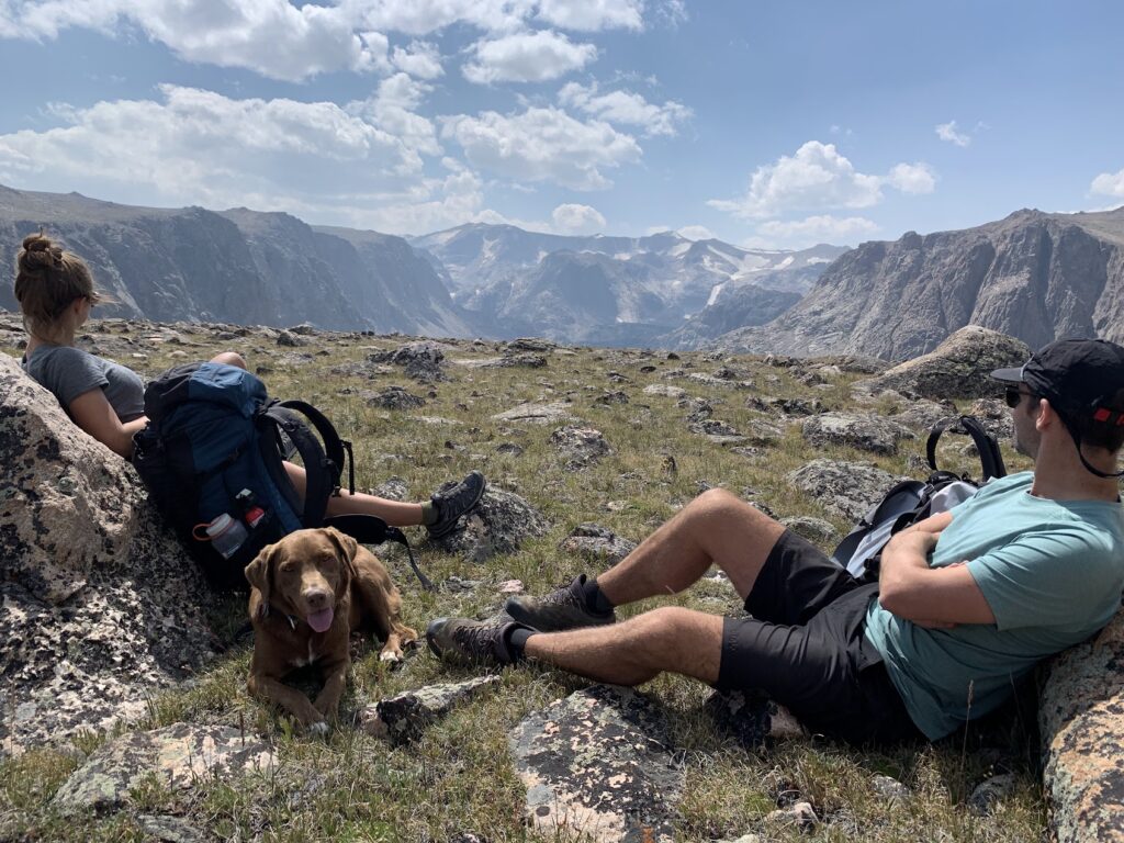 two backpackers and a dog taking a break on the ground