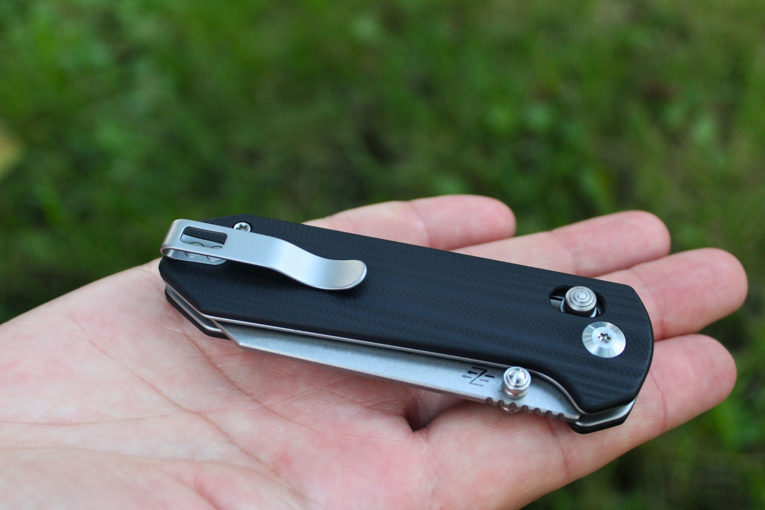 Close up of the Civivi Yonder G10 Pocket Knife sitting on the palm of someone's hand with a grassy background