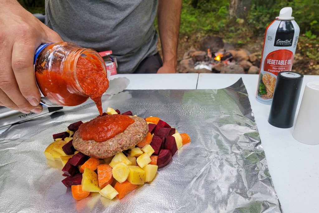 person adding sauce to raw meat atop cut veggetables outdoors