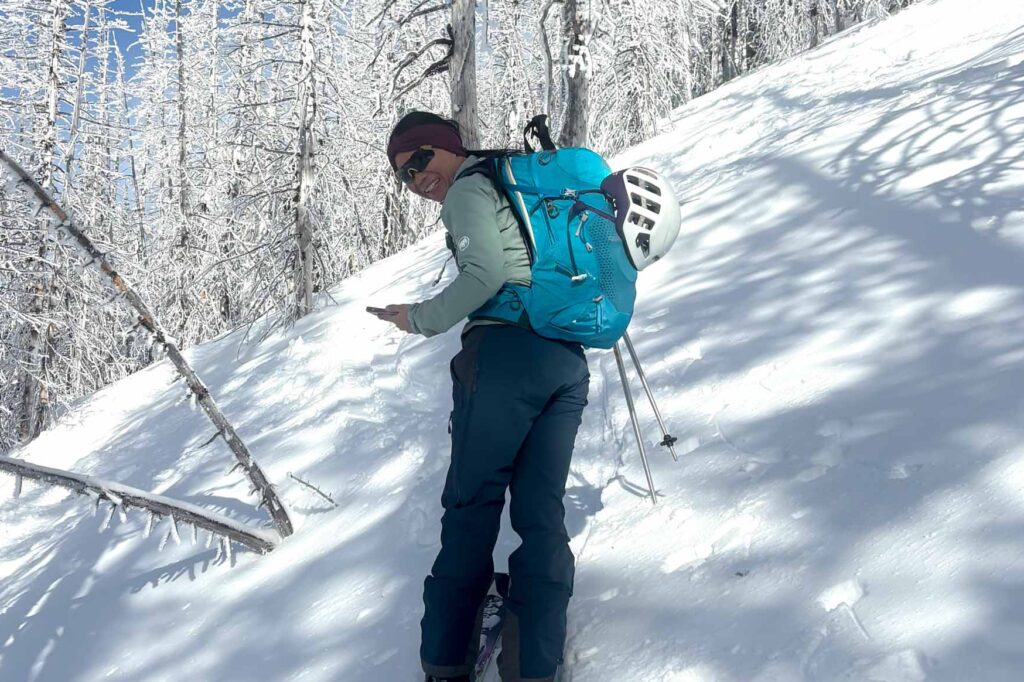 Gregory Juno 24 H2O pack used by a person on skis against a snowy hill with snowy trees on a sunny day