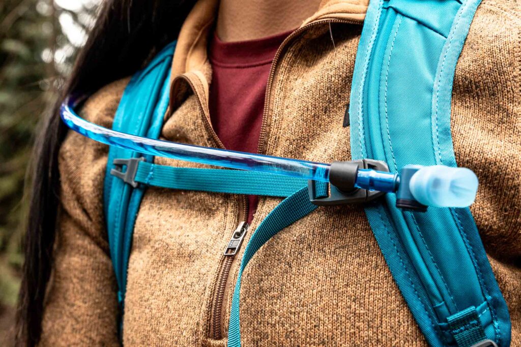 Details of Gregory Swift 16 H2O - a close up view of a person wearing the pack showing the front straps and hydration hose