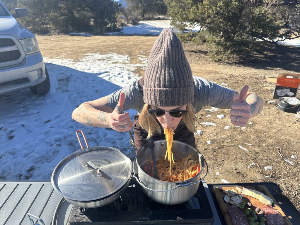 a women wearing a winter hat eats noodles out of the GSI Outdoors Glacier Stainless Troop Cookset