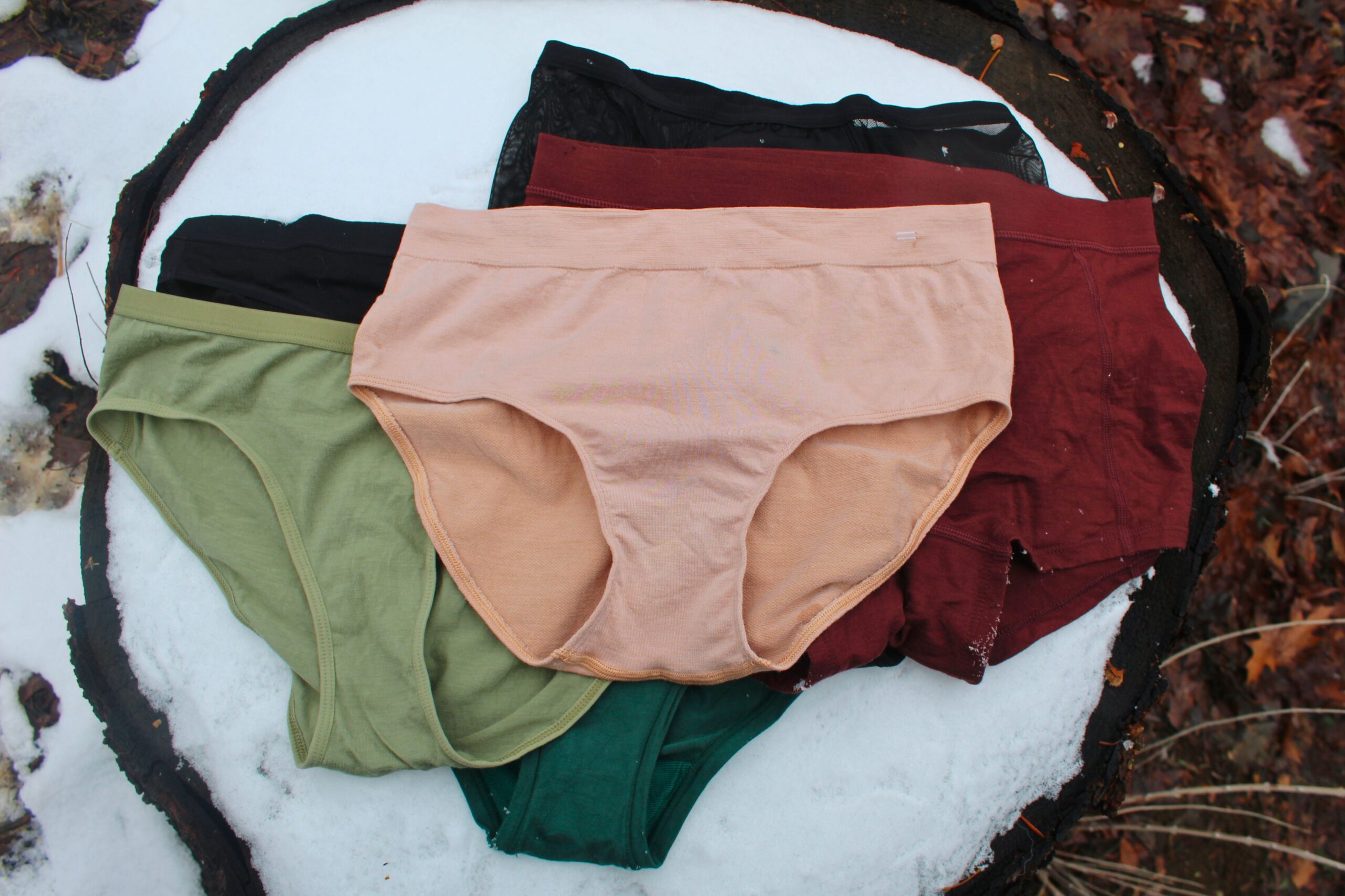 Six pairs of the women's hiking underwear tested laid out on a snowy stump