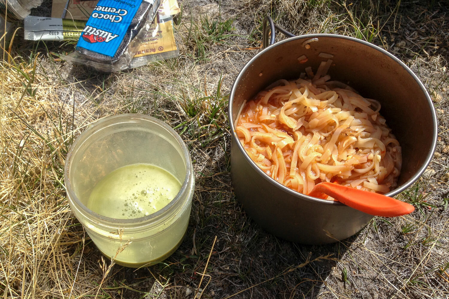 camping meal on the ground consisting of pad thai and matcha