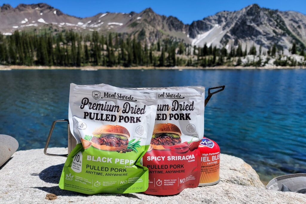 fuel canister and dried meat packages in front of an alpine lake