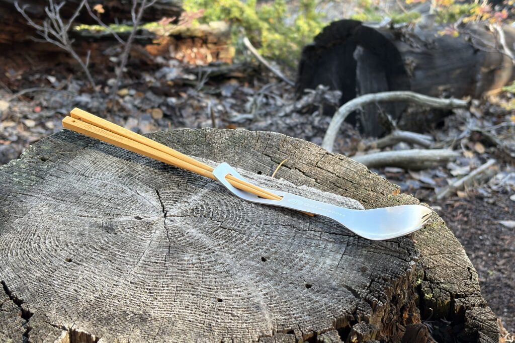 a chopsticks and spork combo sits on a tree stump