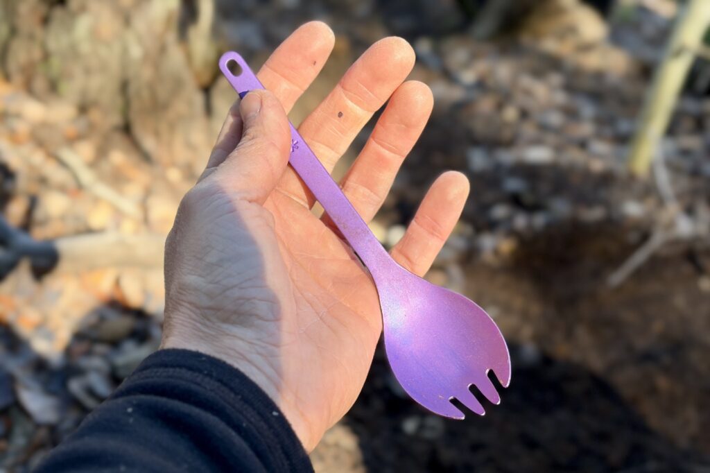 a hand holds a purple titanium spork