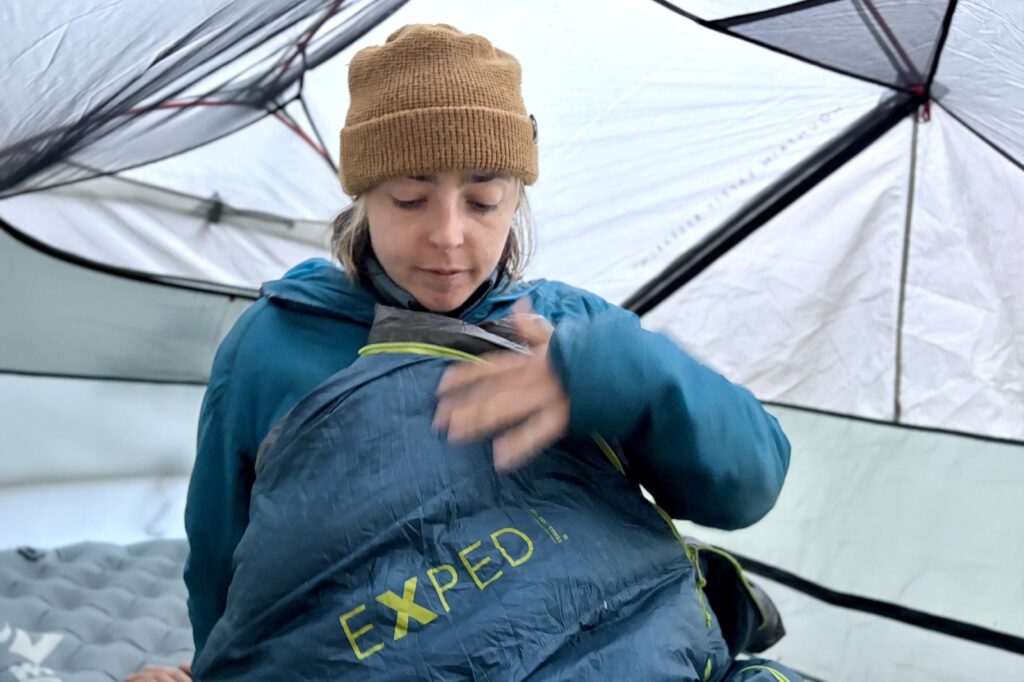 a hiker sits up in a tent while tucked into a blue exped sleeping bag