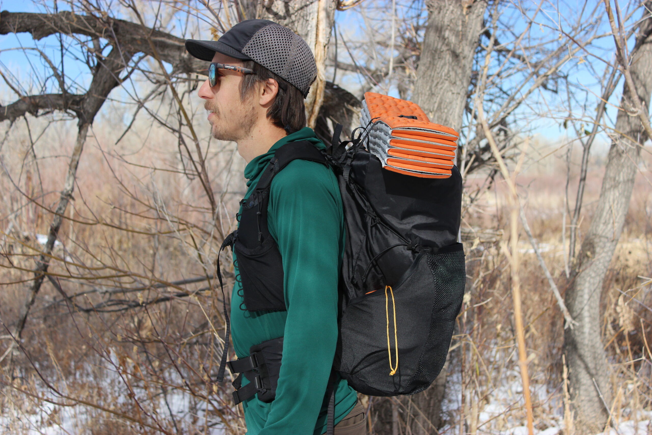 A profile shot of a hiker wearing the Nashville Pack Cutaway with an orange sleeping pad on top.