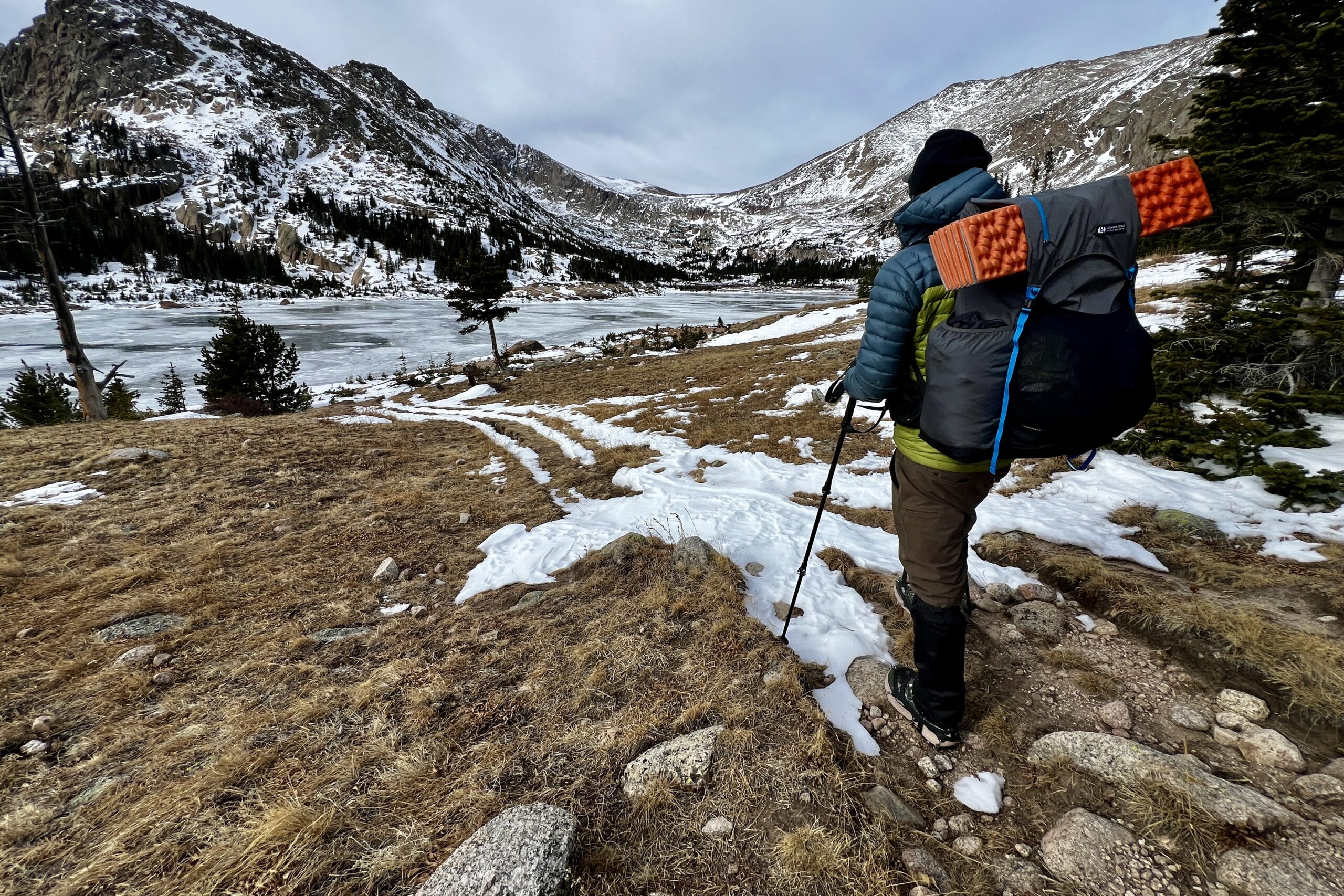 A hiker looks over a frozen lake while wearing a fully loaded backpacking backpack.