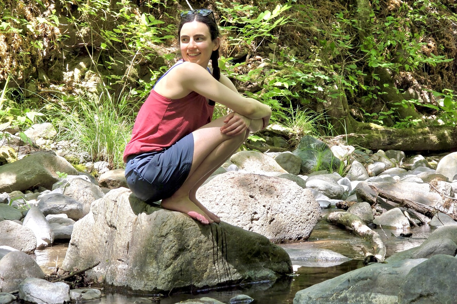 Woman squats on a rock in the middle of a creek.
