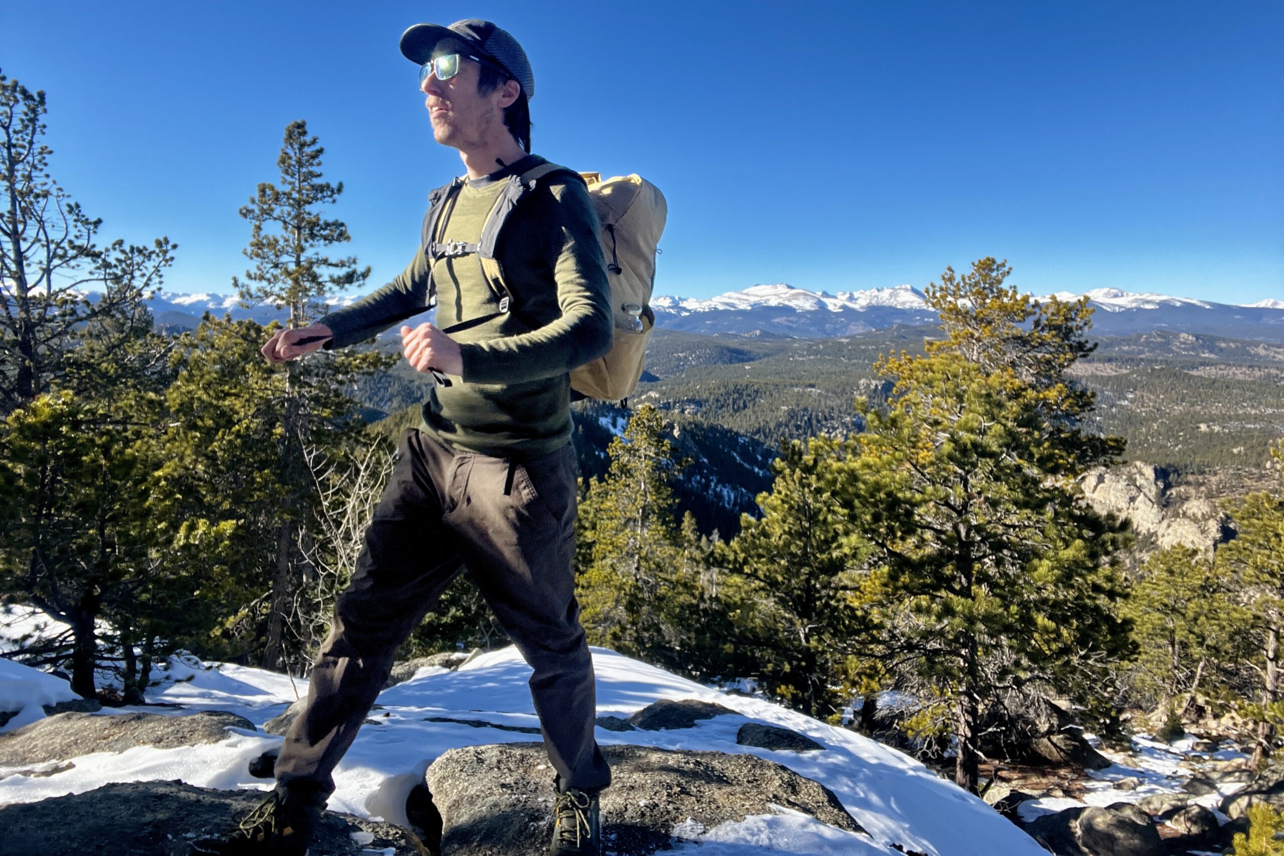 A hiker tightens the straps on a backpack while wearing it and the Smartwool Intraknit. Sky, mountains, and trees in the background.