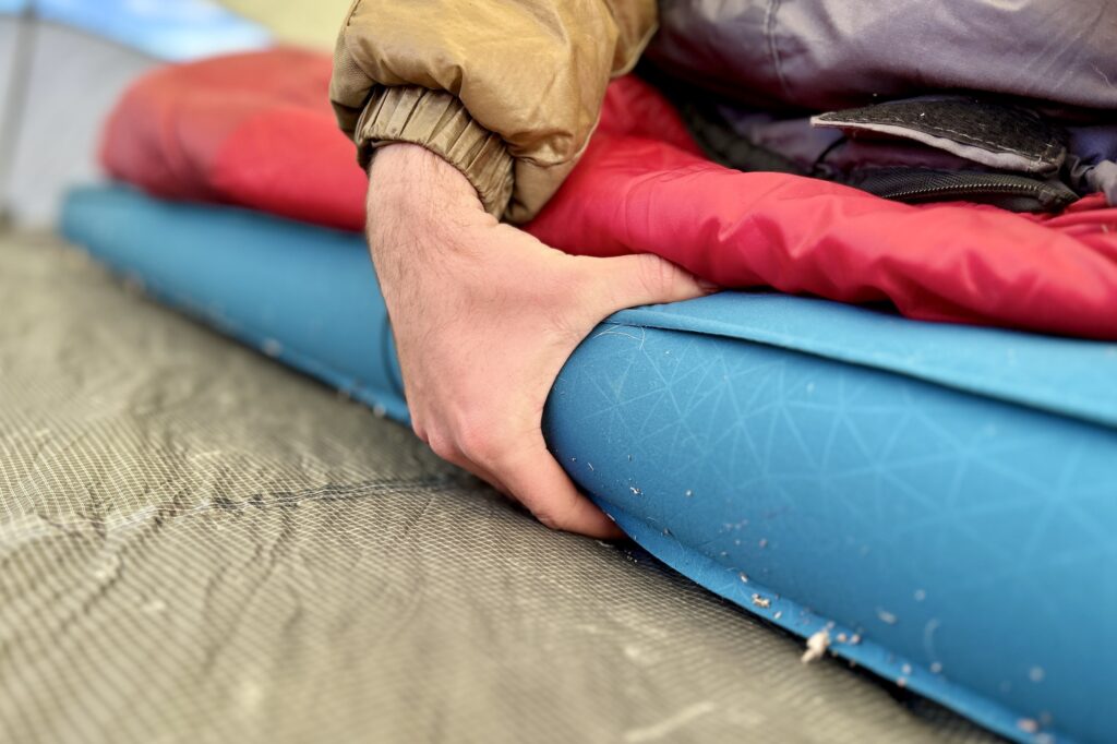 A hand grasps the side of a thick camping mattress.