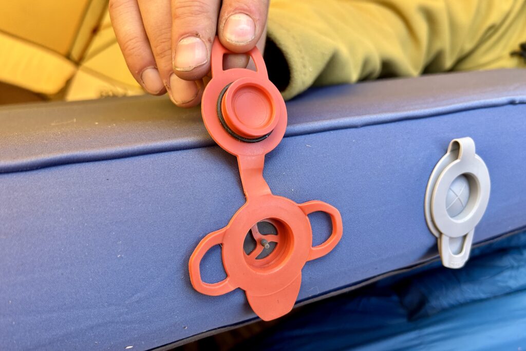 Close-up image of an intake and dump valve on a camping mattress. A hand holds open the intake valve.
