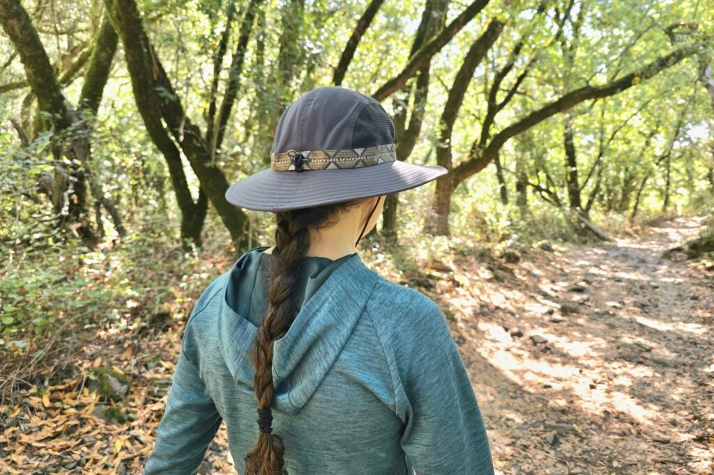 Woman hikes along a forested trail wearing a sun hat.