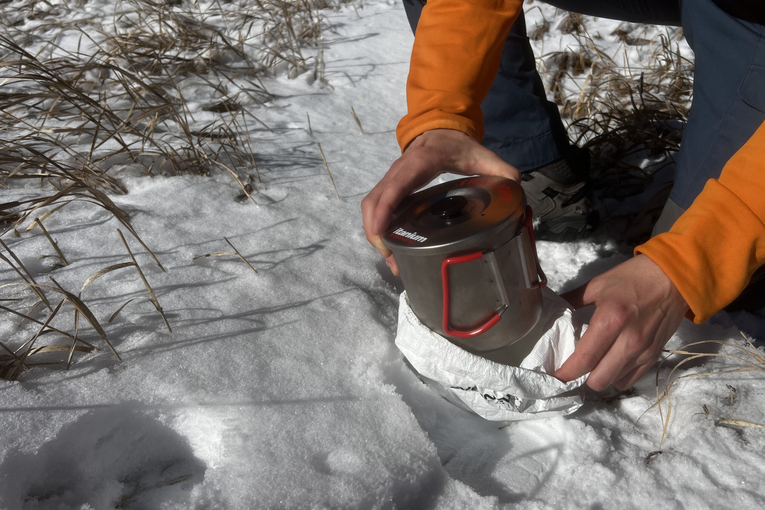 A hiker stores the evernew pasta pot in its white stuff sack against a snowy background.