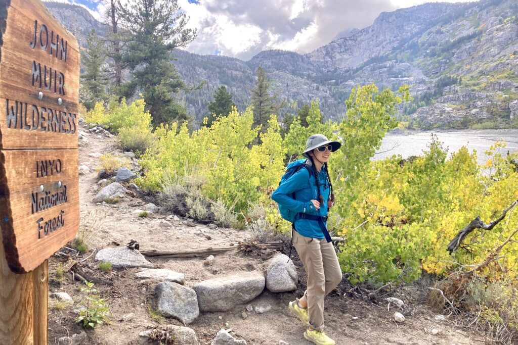 A woman hikes down a trail lined with aspens.