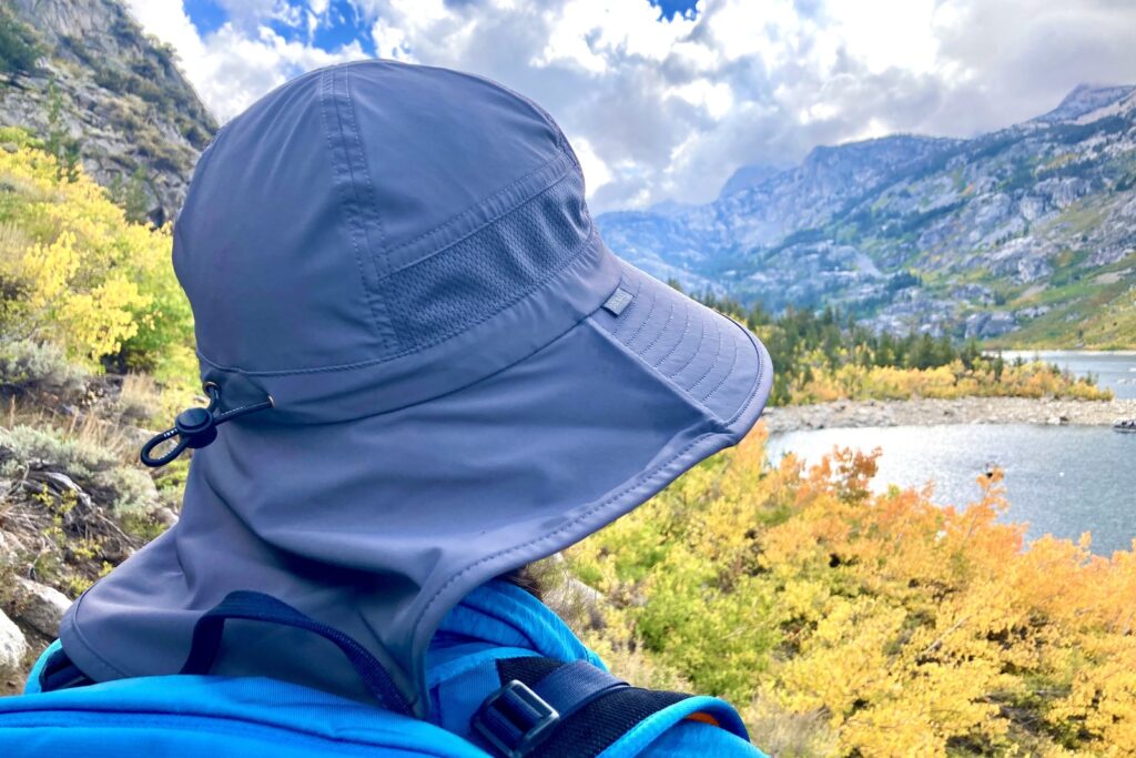 A woman looks at an alpine lake surrounded by golden aspens while wearing her sun hat.