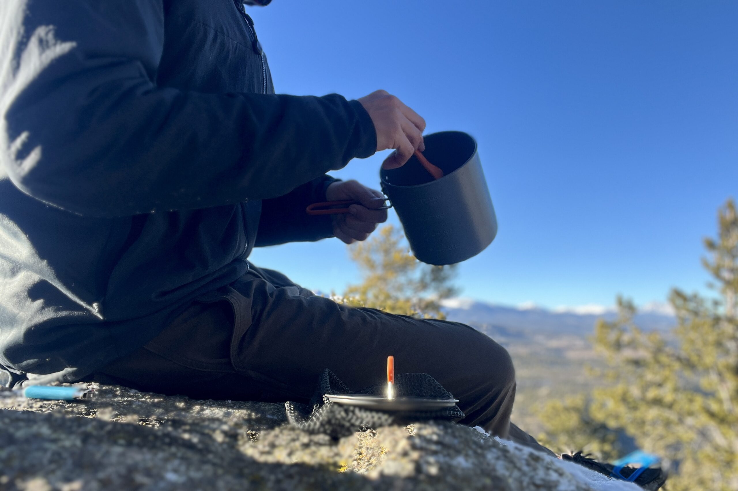 A hiker sticks a fork into the GSI halulite boiler pot with a mountain background.