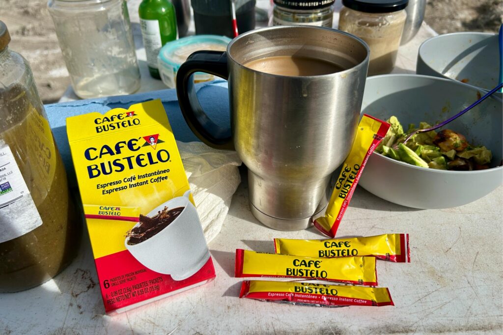 Up-close image of a metal mug with Cafe Bustelo coffee packets around it and food on a table