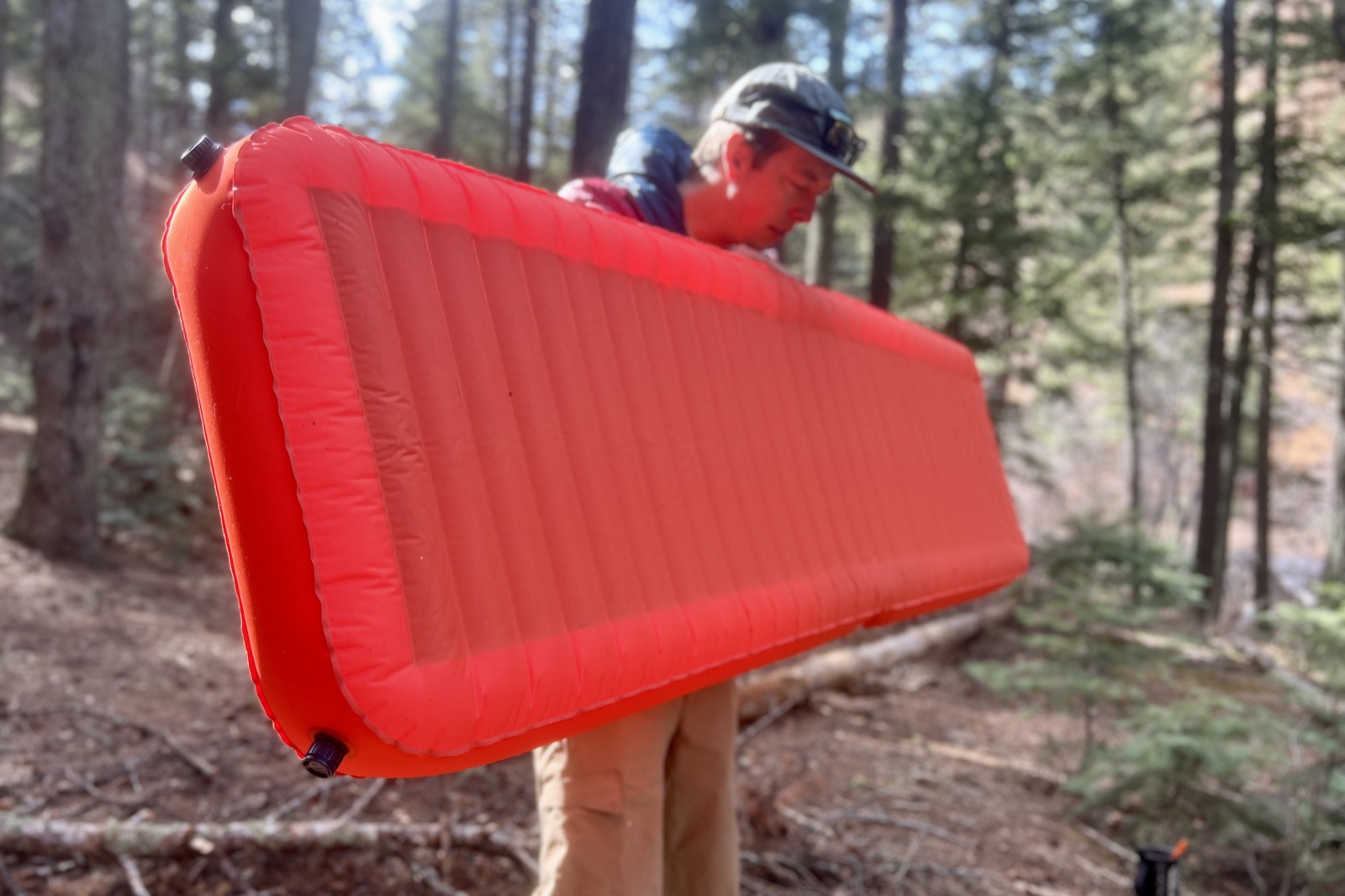 a hiker holds an inflated red sleeping pad in the middle of the woods