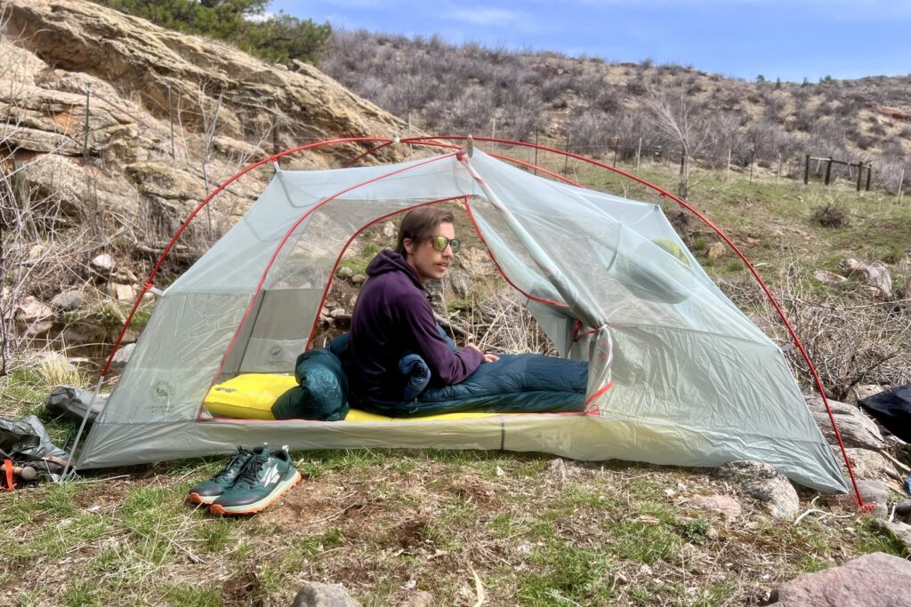 A hiker sits in a ten with the doors open and fly off