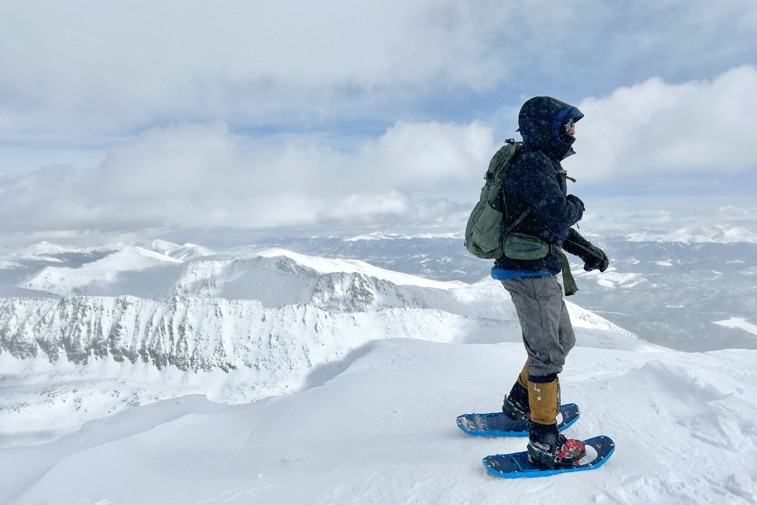 A winter hiker wearing snowshoes on an overlook in a snowy mountain scene.