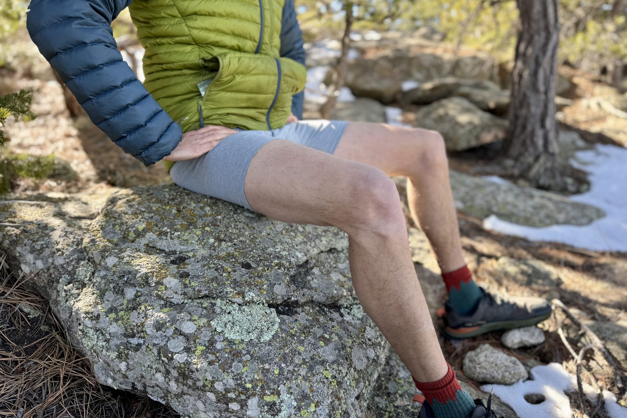 A hiker sits on a rock wearing a puffy jacket and pair of under armour underwear.