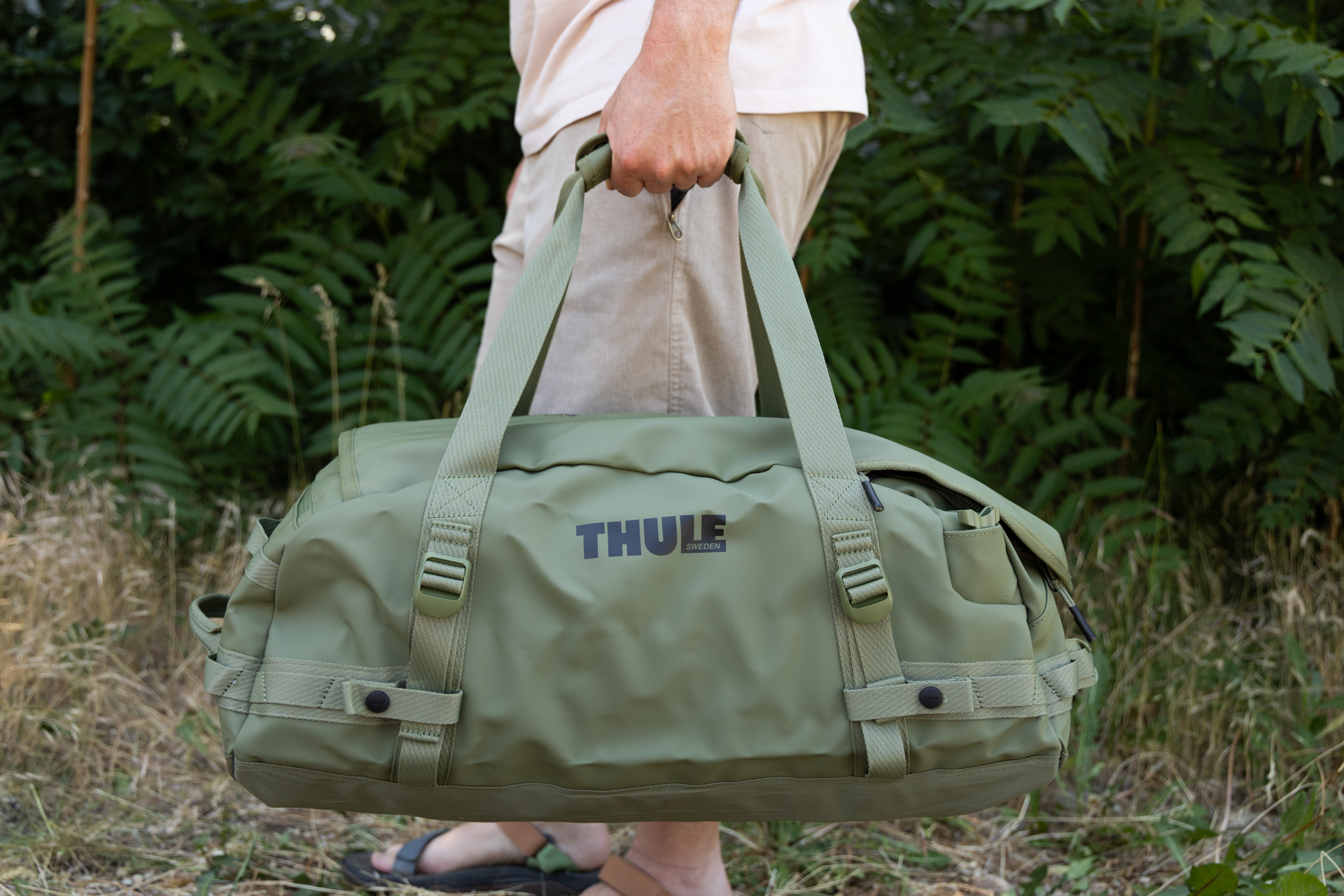 A man carries the Thule Chasm 40L duffel bag by the grab handles. The bag hangs next to his legs.