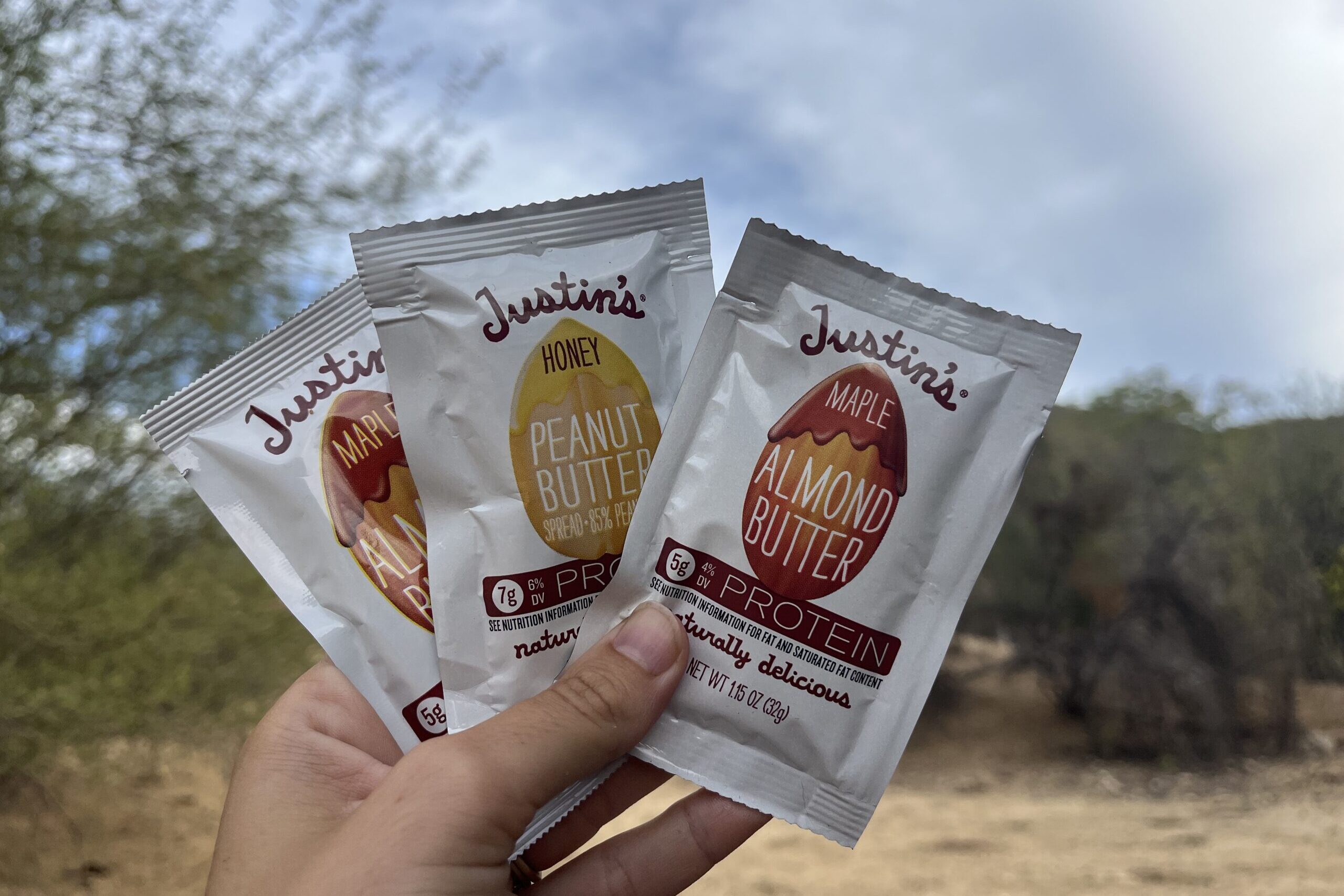 hand holding up Justin's Nut Butter Pouches in mountainous setting