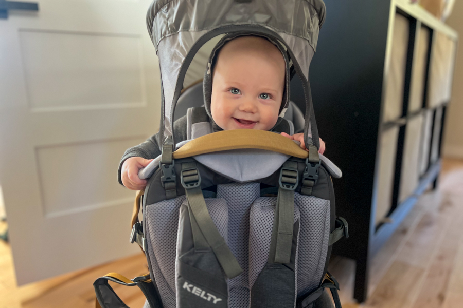 Smiling baby seated comfortably in the Kelty PerfectFIT Journey Elite carrier indoors.