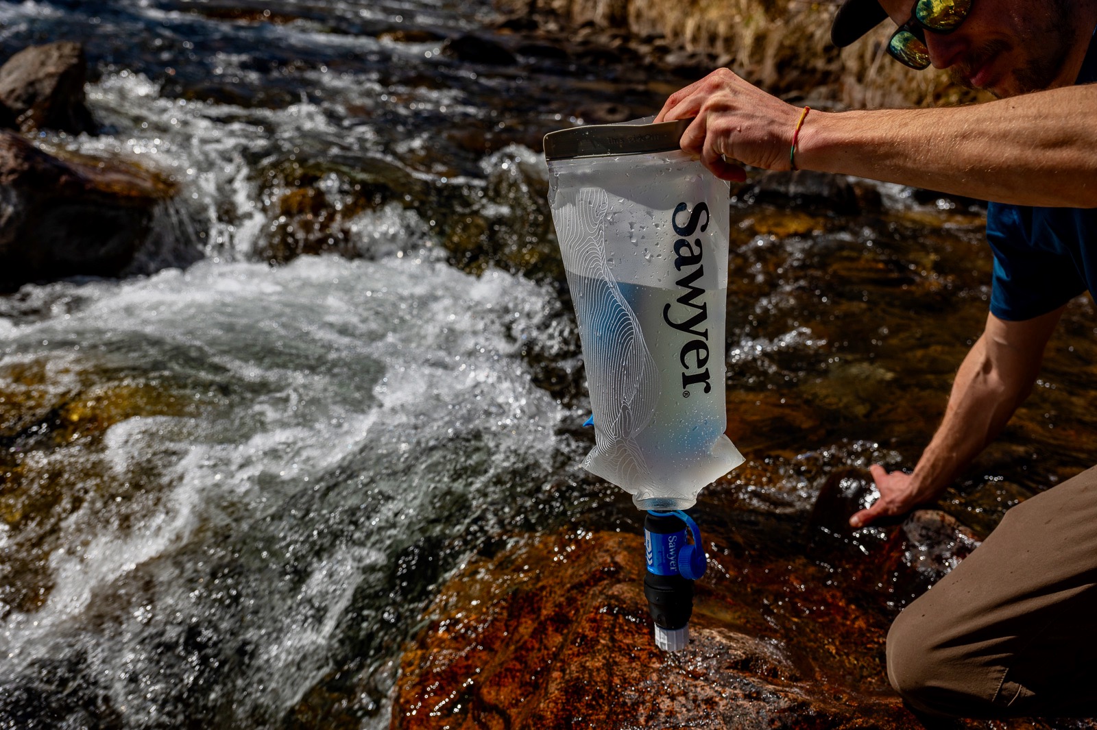 A hiker holds a bladder with the sawyer squeeze attached next to a creek