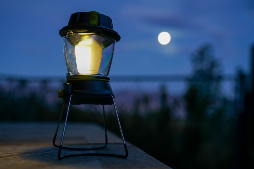 The GoalZero Lighthouse 600 lantern sits on a table with half its bulb illuminated. A full moon is in the background.