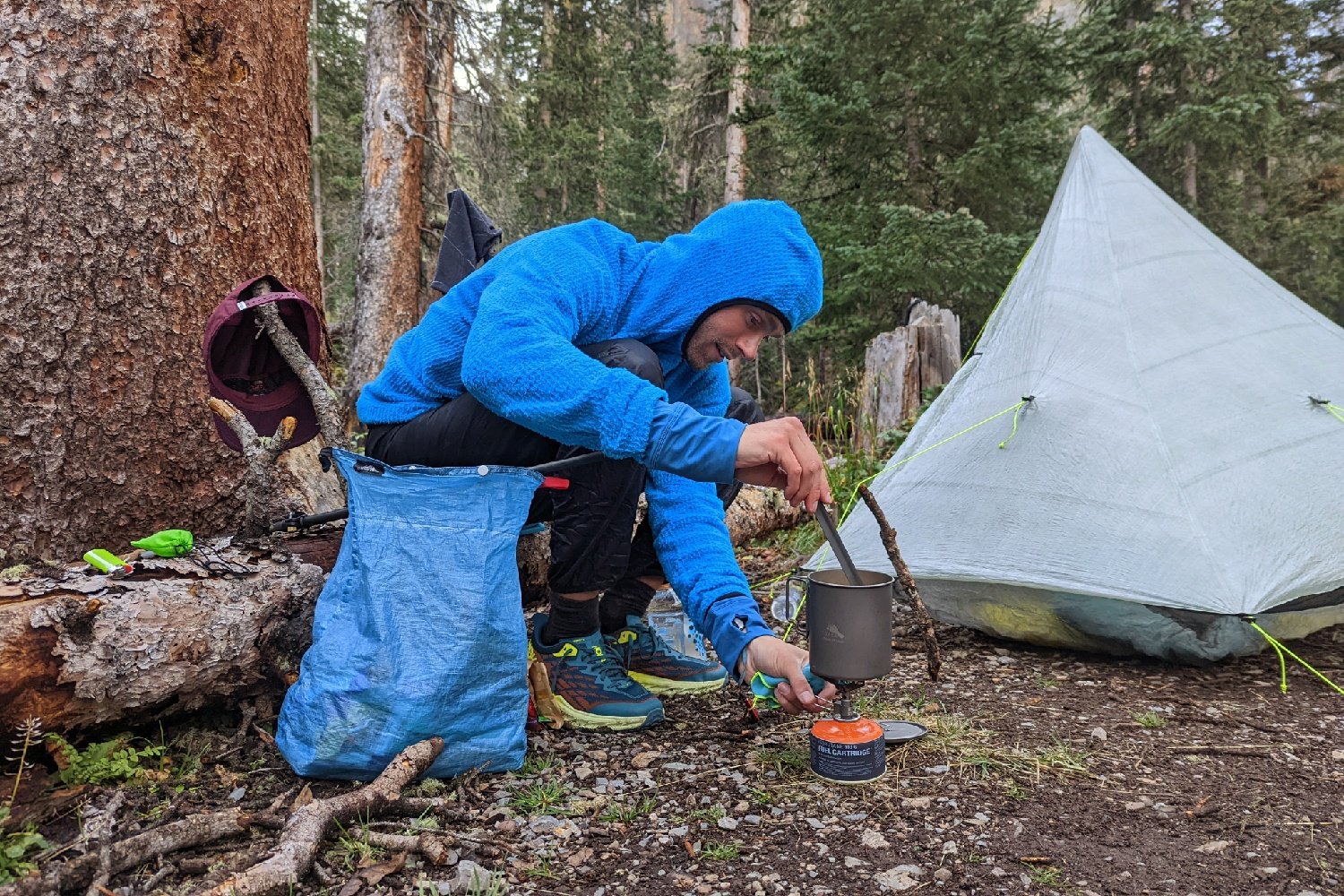 a backpacker making food in campnext to their tent with an ultralight food bag stuff sack next to them
