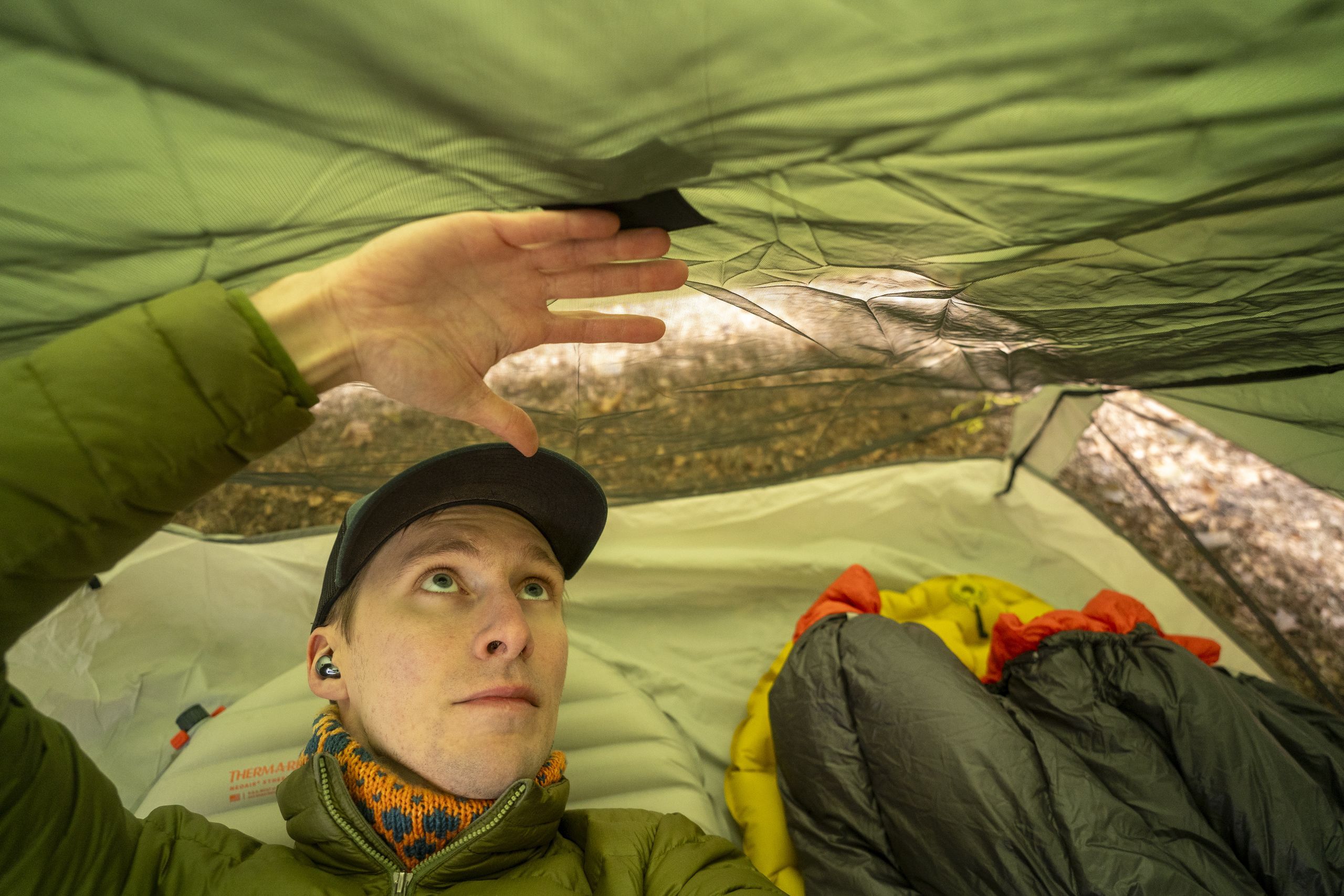 A man in a green jacket lays down in a tent