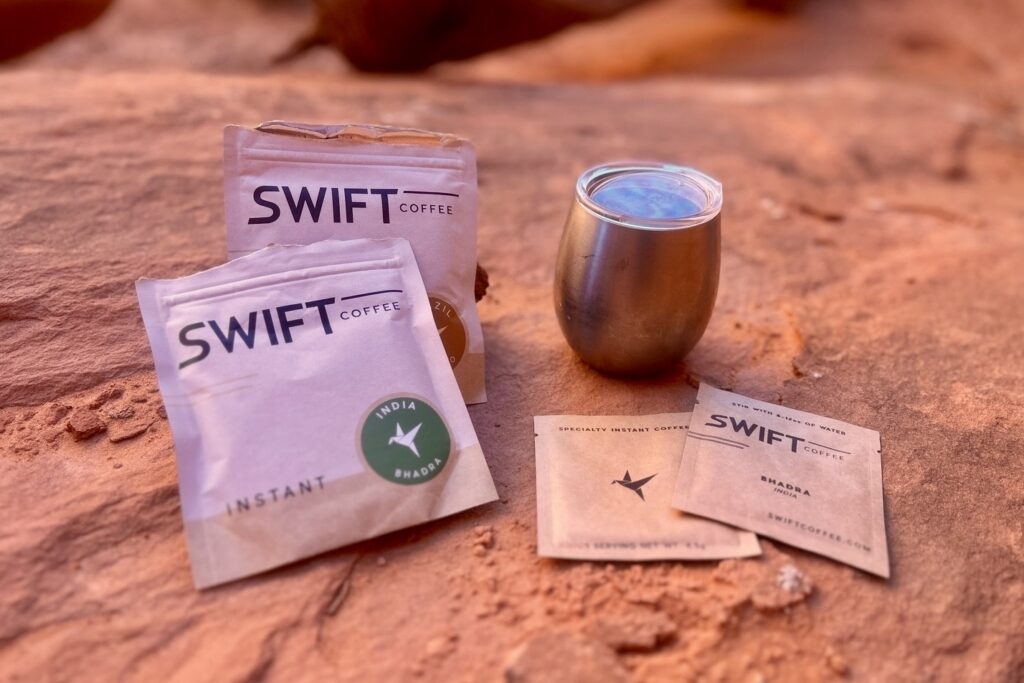 Packets of Swift brand instant coffee in a desert setting next to a mug.