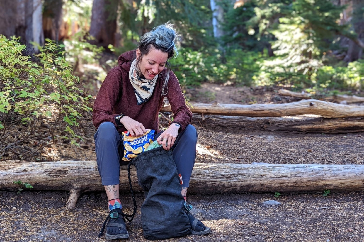 hiker putting fritos in her ursack bear bagwhile sitting on a log