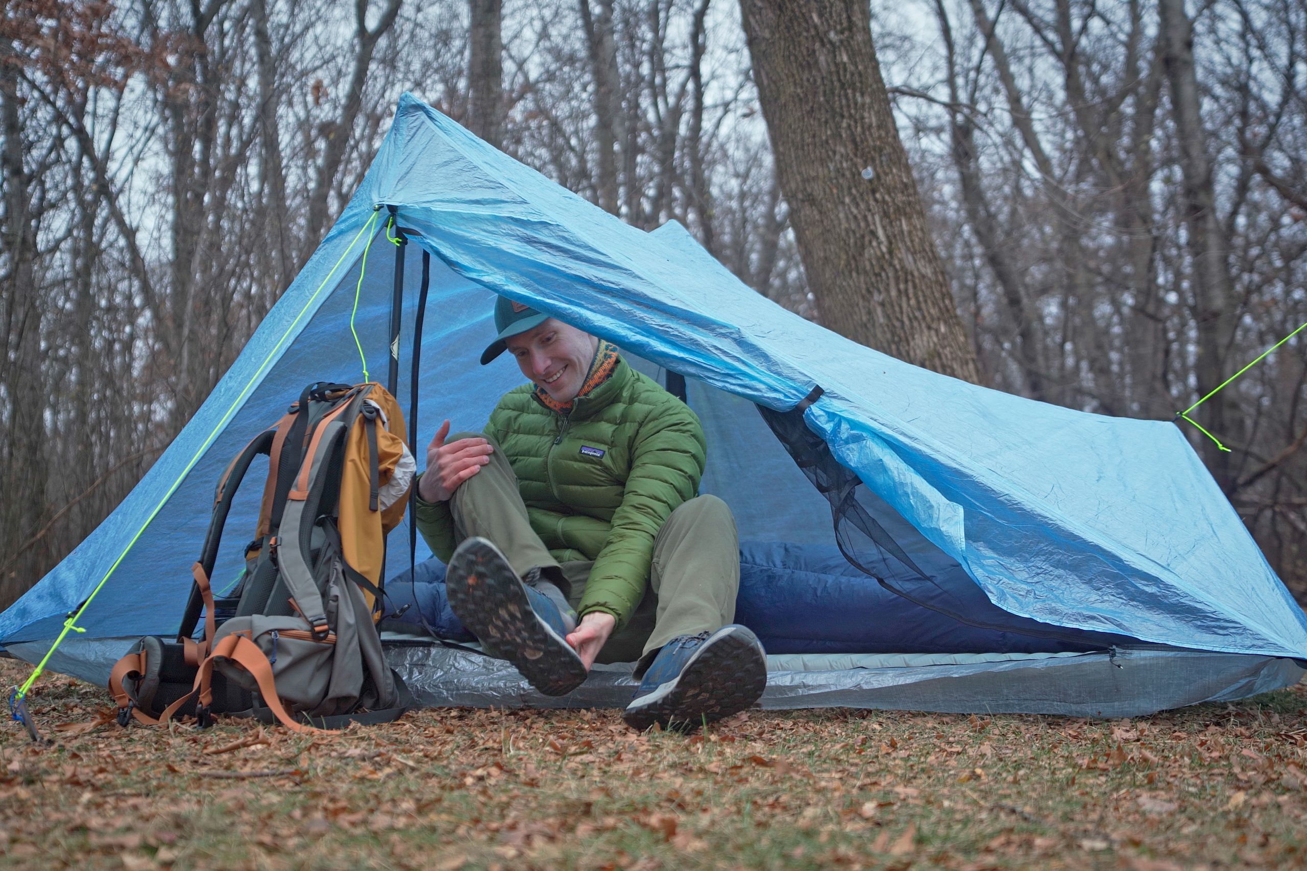 a man in a green coat sits in a blue tent