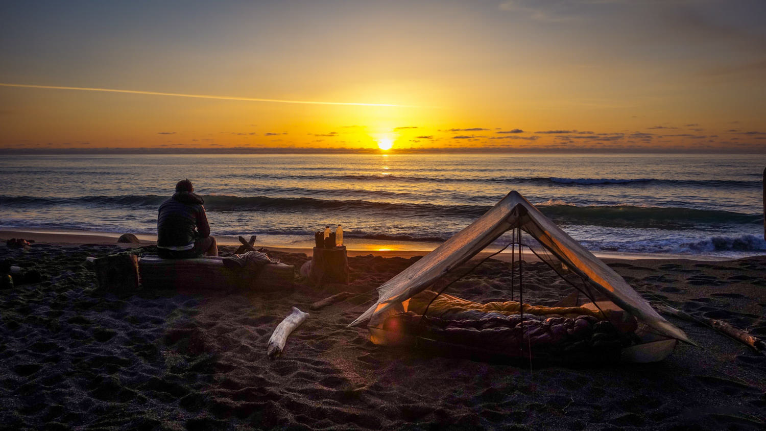 a person watching the sunset on the beach with their zpacks duplex tent pitched next to them